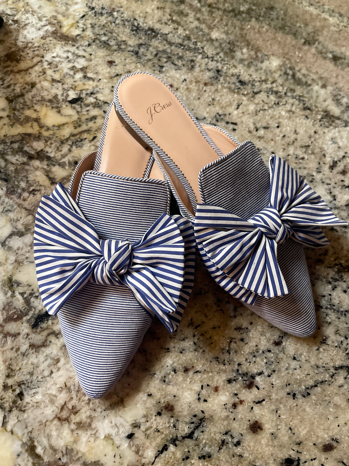 J.Crew pointed-toe bow slides featuring a blue-and-white striped pattern and a large fabric bow on top.