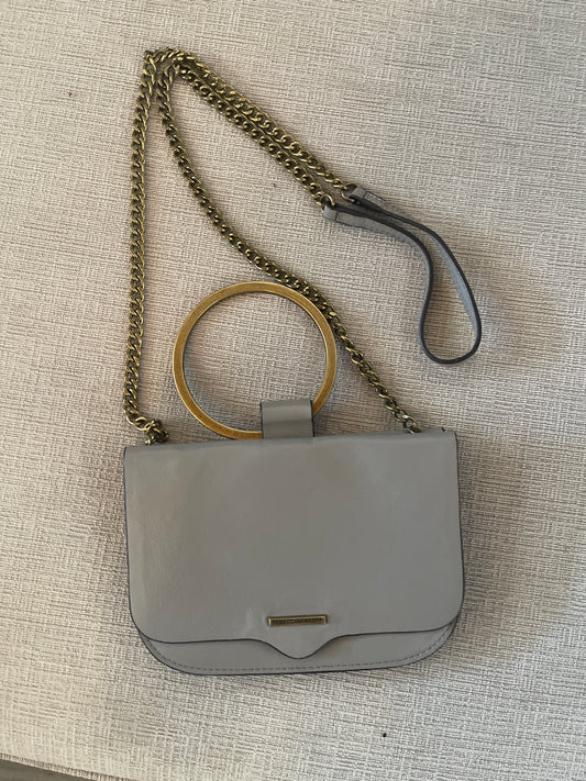 The handbag pictured is the Rebecca Minkoff Ring Crossbody (often referred to as the Ring Clutch or Wristlet) in a taupe or light grey leather with antiqued gold-hardware and top ring handle.
