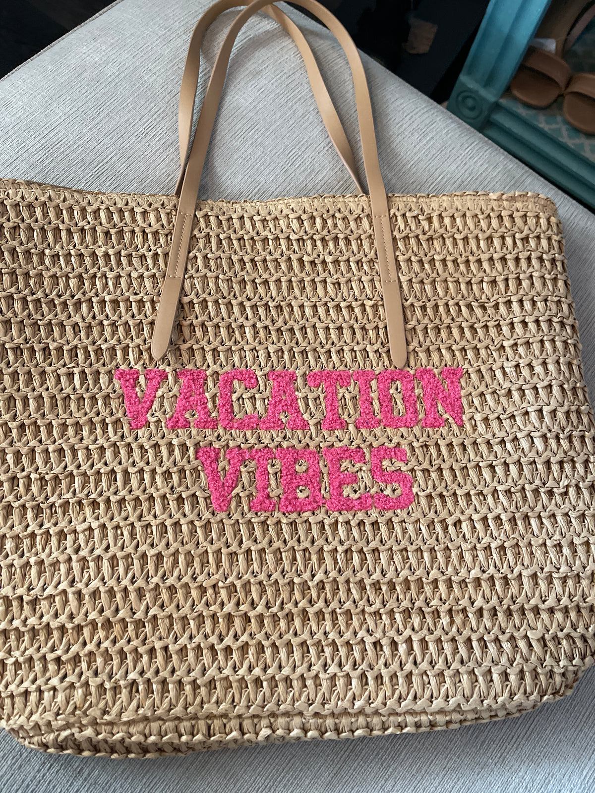 woven straw tote bag features bright pink embroidered lettering that reads "VACATION VIBES"