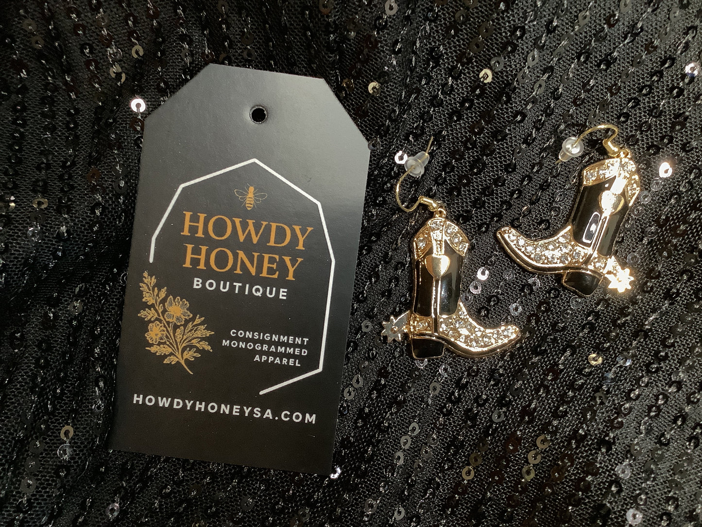 Cowboy boot earrings with rhinestones on a black sequined background, accompanied by a 'Howdy Honey Boutique' tag.