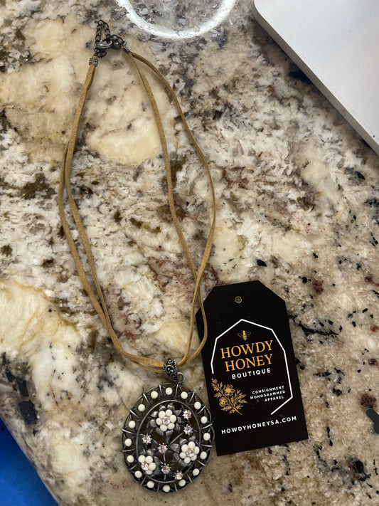vintage-style silver-tone oval medallion necklace featuring white floral and crystal rhinestone details on a tan cord.